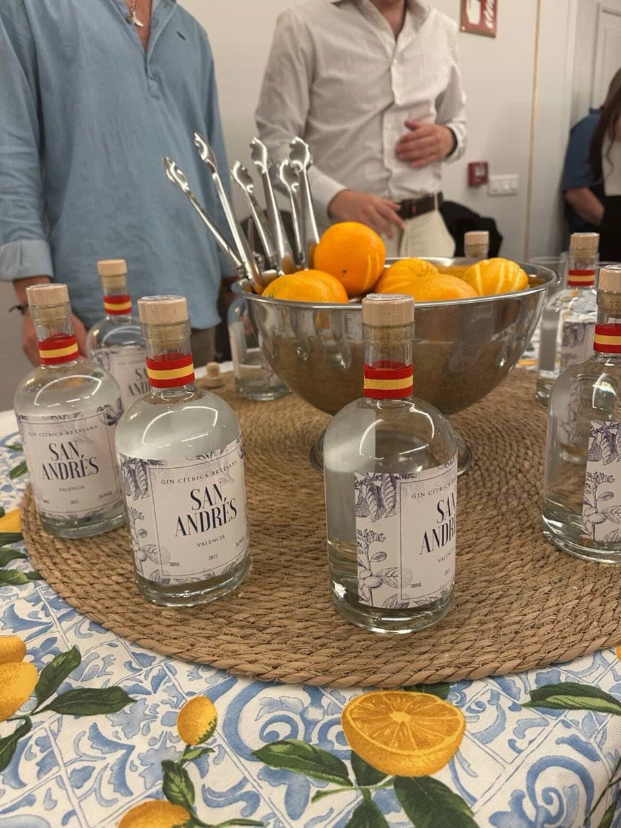 Botellas de San Andrés y un cuenco de naranjas sobre un mantel con naranjas